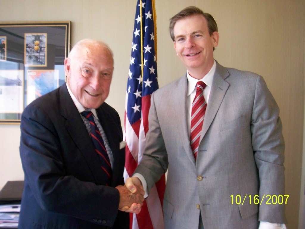 Admiral 'Ace' Lyons shaking hands with Dr. Joe Arminio in front of an American flag